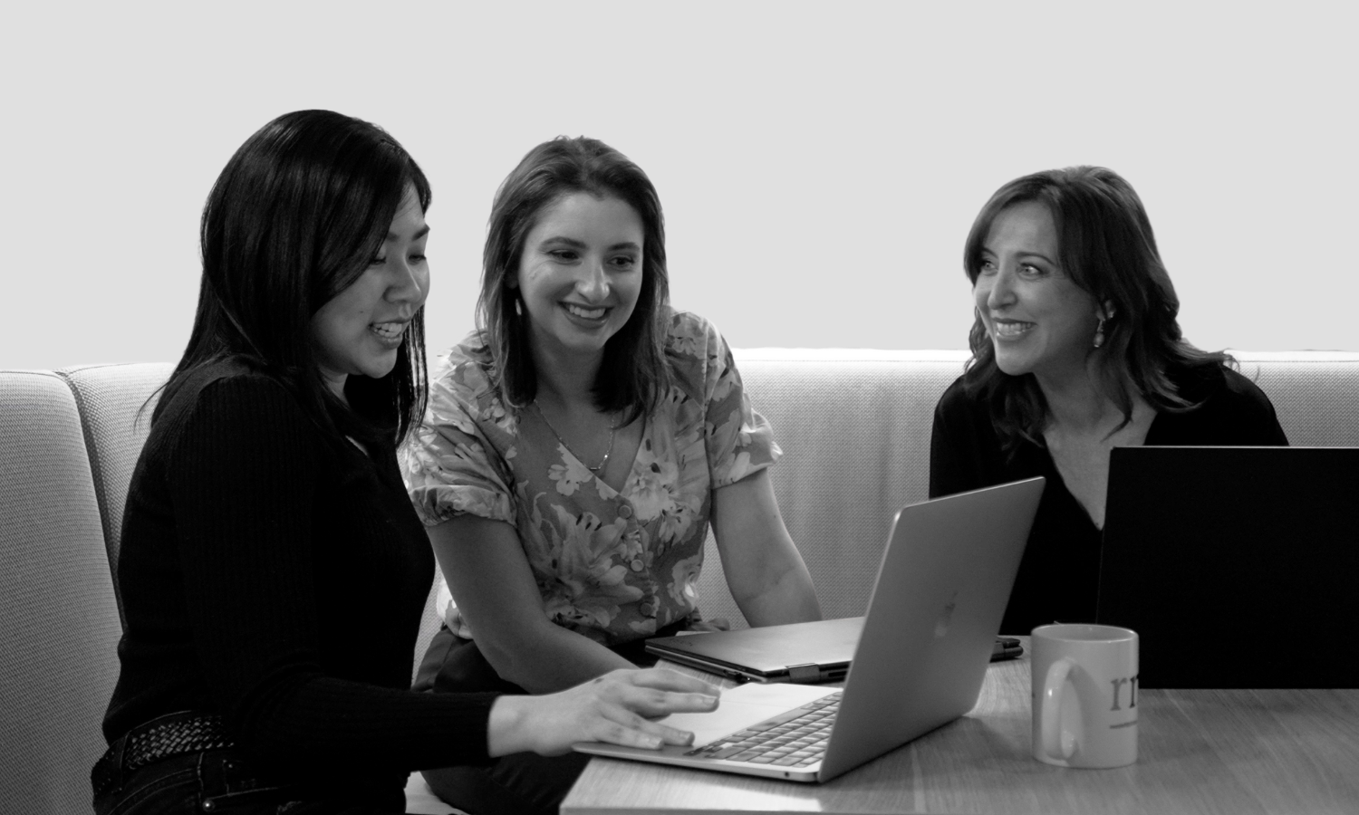 Three women happily sharing a laptop screen at a desk