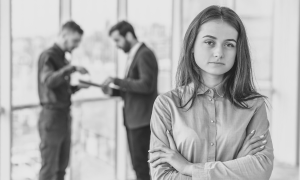 Sad woman in workplace with men talking behind her, black and white
